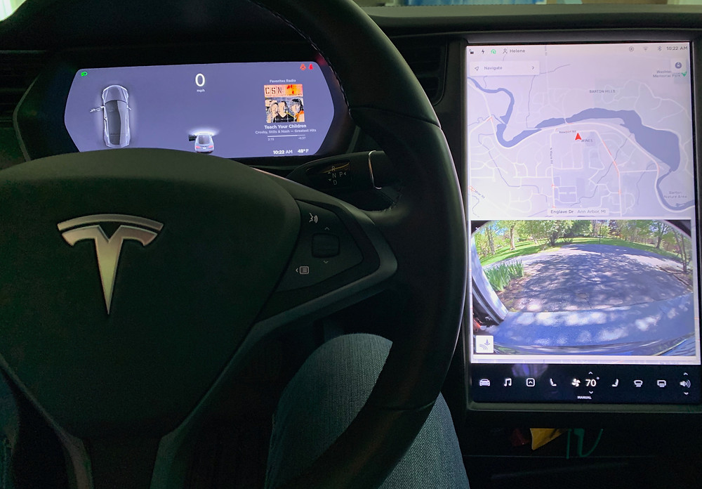 Driver display of speed and car, infotainment screen with map and rear camera image.