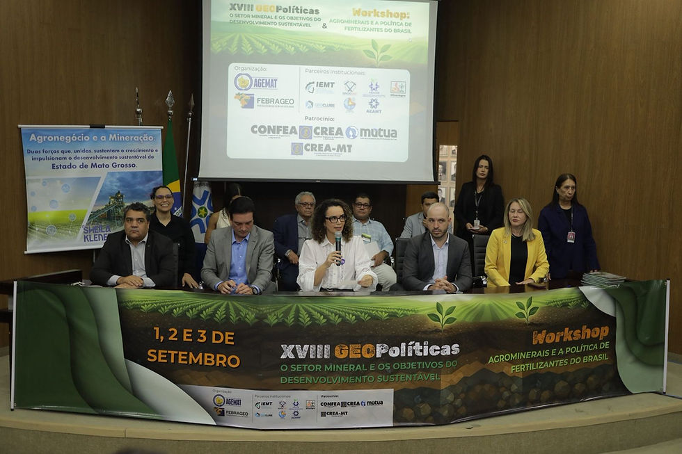 Vista frontal de uma mesa de palestrantes durante o evento "XVIII GEOPolíticas" e "Workshop Agrominerais e a Política de Fertilizantes do Brasil". Uma mulher no centro da mesa discursa ao microfone, ladeada por outros participantes. Ao fundo, um telão exibe os logotipos dos organizadores e parceiros.