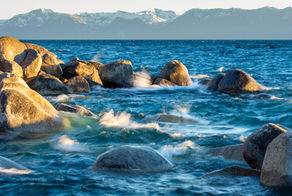 Waves breaking on sunlit rocks with mountains