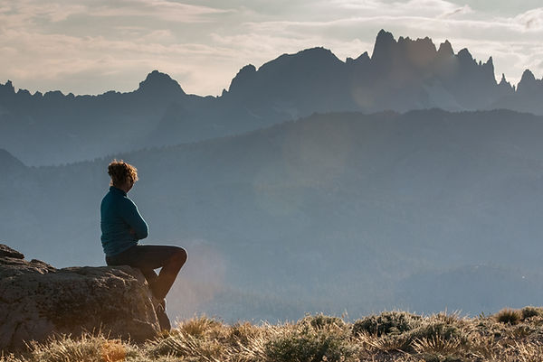 A girl sits on a rock staring off to the distant jagged mountain peaks
