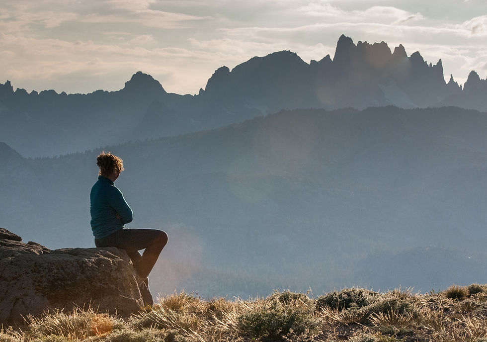A girl stares off to the distant silhouetted jagged mountain of the Sierra Nevadas including the Minarets, Ritter, and Banner.