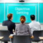 Three people sit facing a turquoise board with "Objective Setting" text. They're in a classroom setting, ready for a discussion.