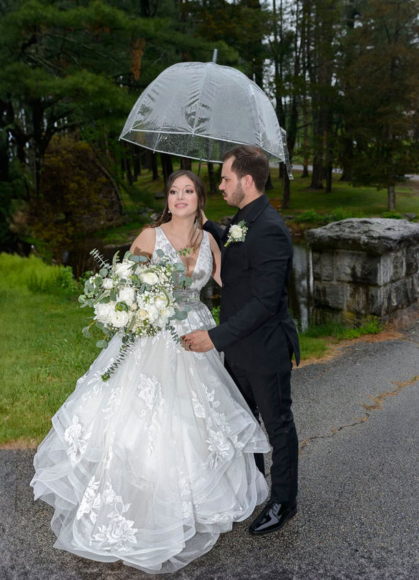 Bride and groom smiling at the camera under clear umbrellas