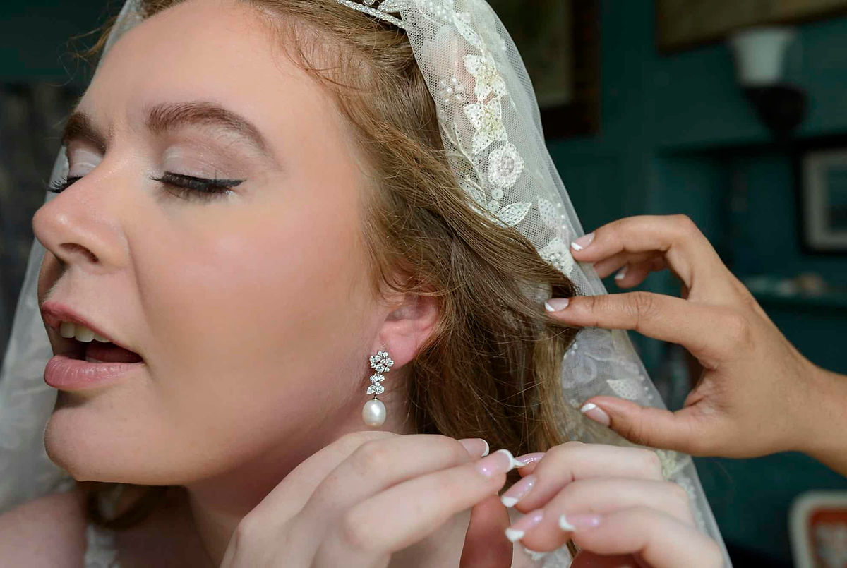 A close-up of a bride getting ready on her wedding day as she puts on pearl drop earrings. Wedding at the USA Space Agency Base in CT.