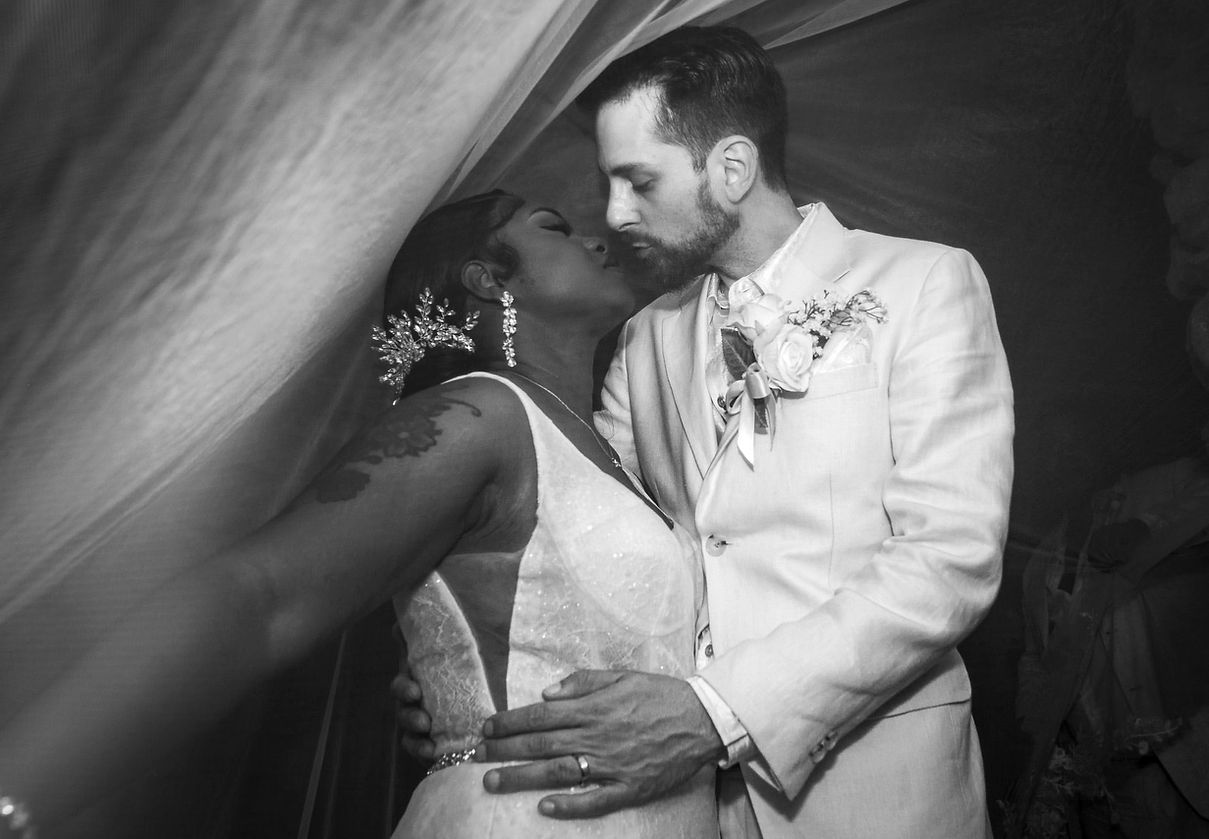 Bride and groom share an intimate embrace beneath a flowing veil in black and white.