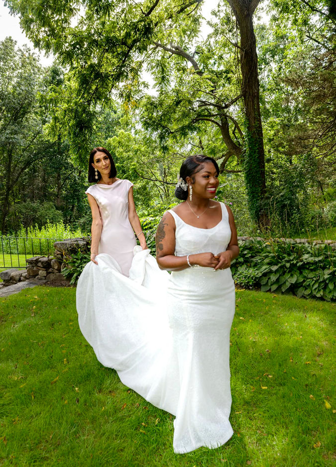 Bridesmaid holding the train of the bride’s dress as she walks toward the ceremony