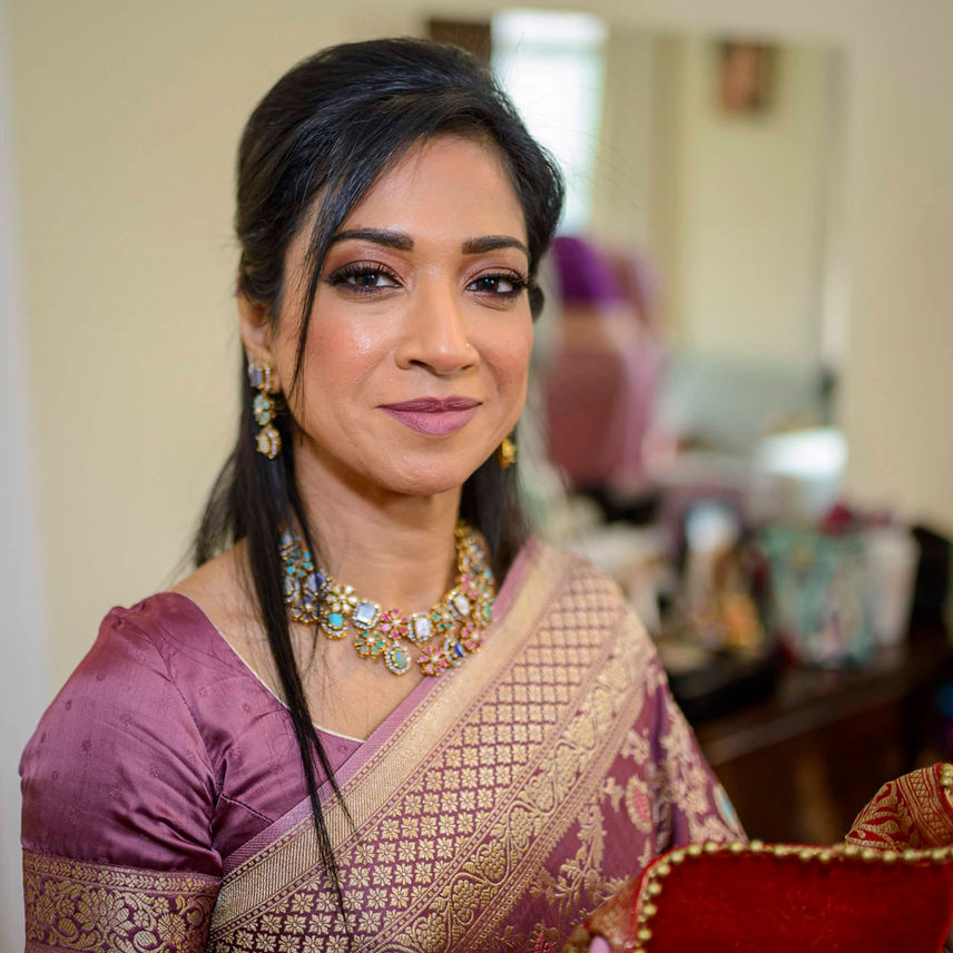 Bangladeshi bride smiling after her makeup is complete, showcasing her gold and ruby jewelry,