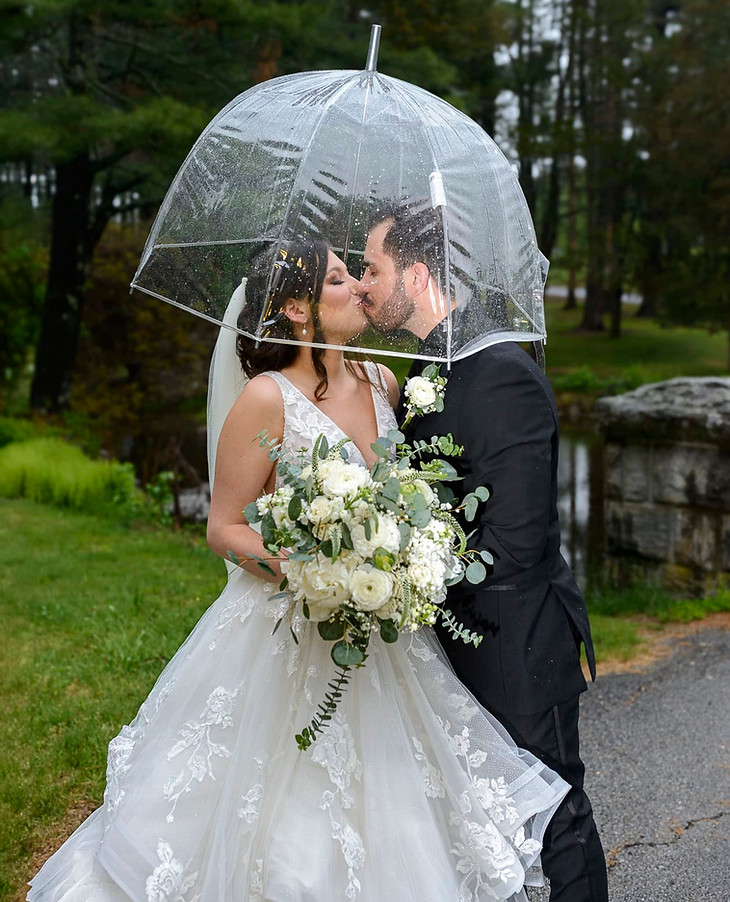 bride-groom-by-pond-kissing-under-a-clear-umbrella.jpg
