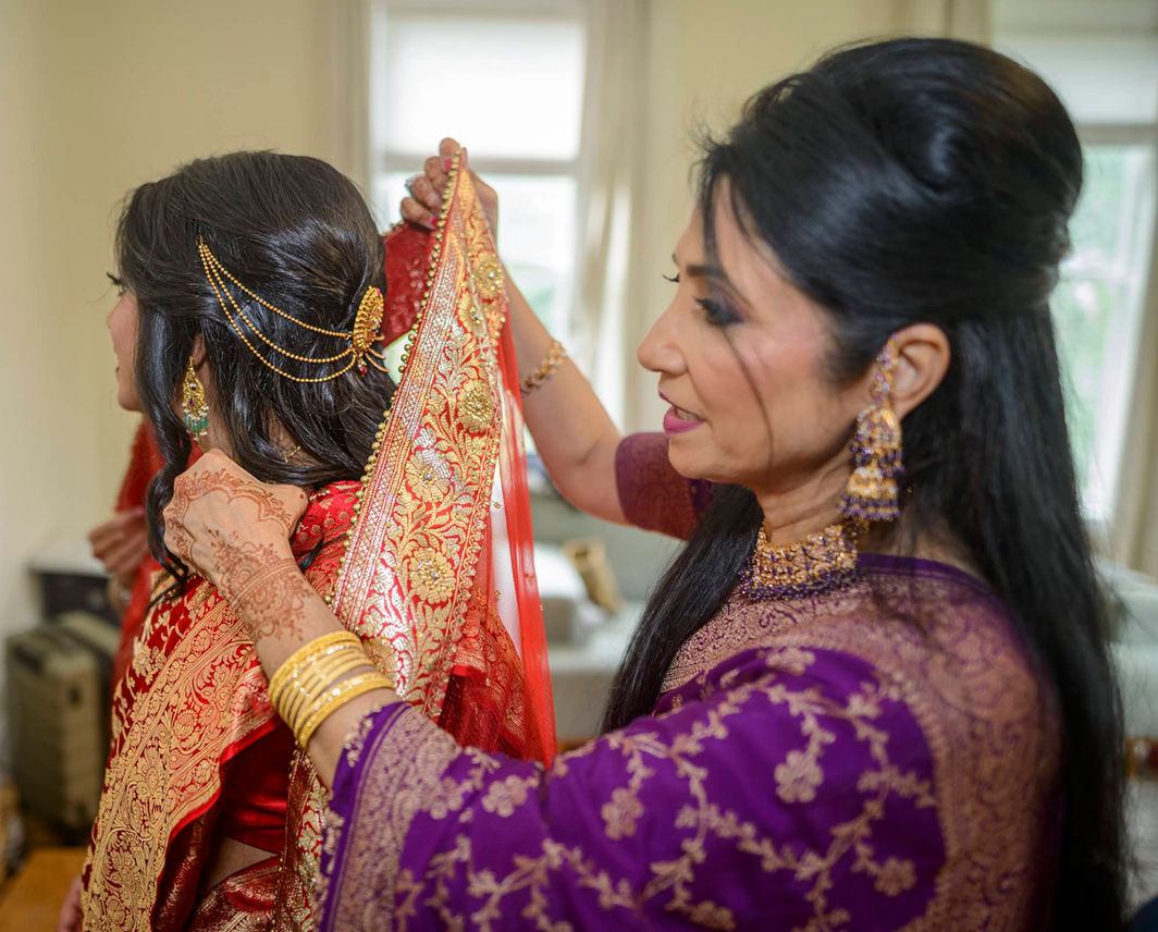 Mom adjusting the bride’s red and gold saree during the traditional getting ready moments.