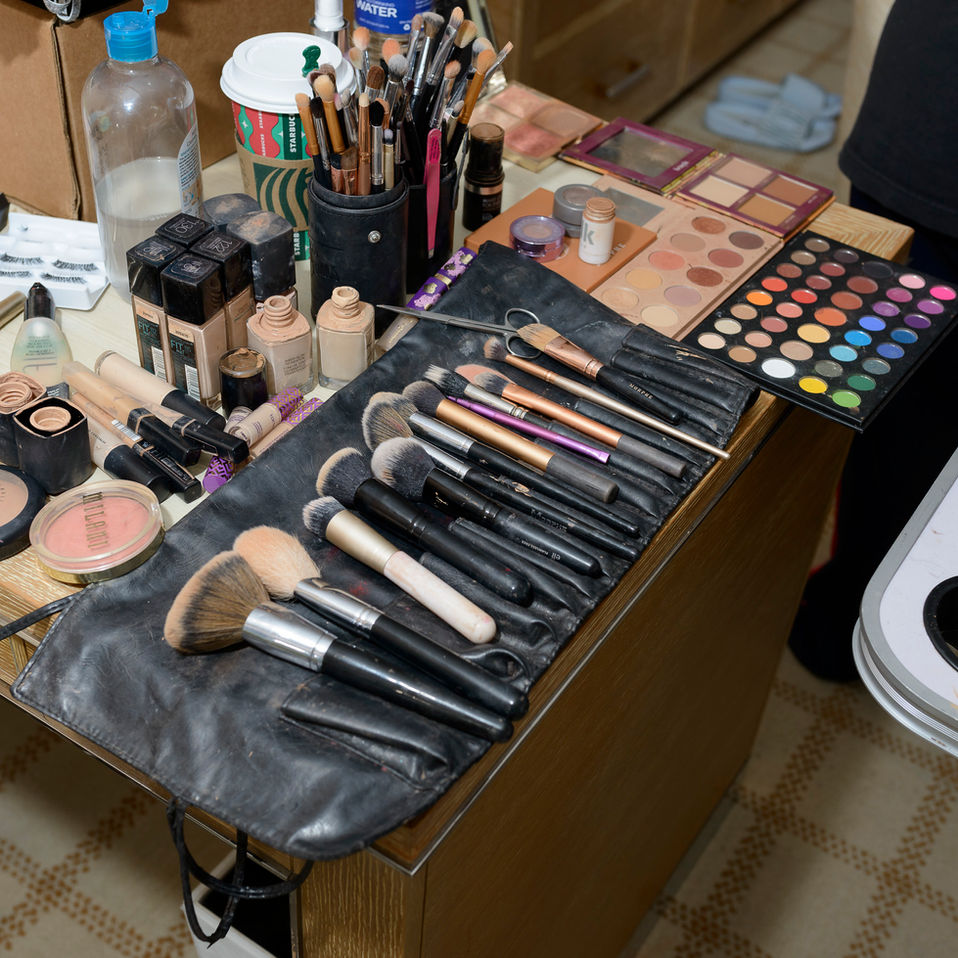 Makeup artist's tools. A collection of professional makeup products and tools neatly arranged on a wooden table, including makeup brushes, eyeshadow palettes, foundation bottles, blushes, and beauty sponges, ready for use during a wedding preparation.