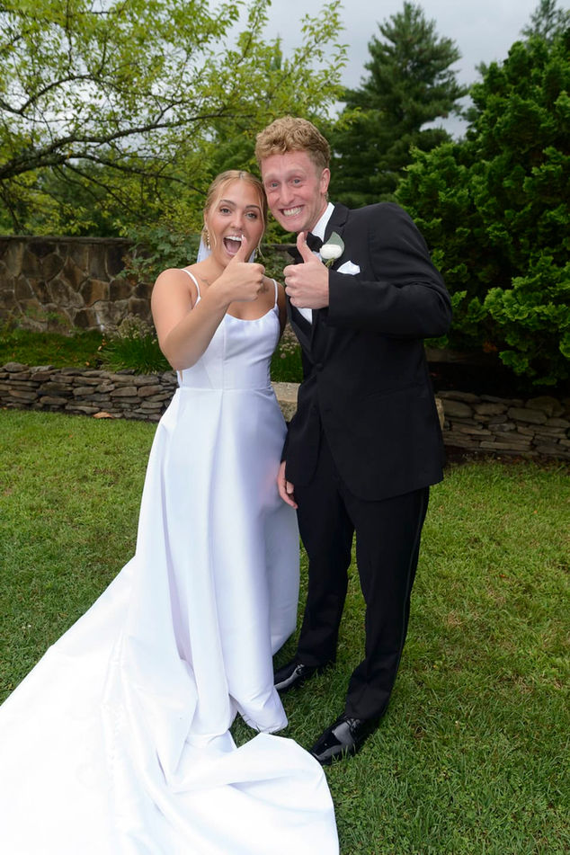 Bride and groom smiling and giving thumbs up in full length garden portrait.