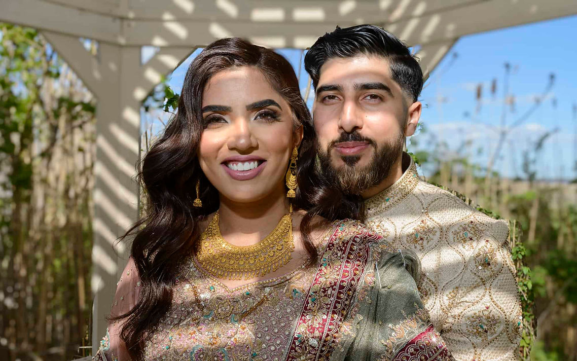 Pakistani bride and groom pose together in elegant Pakistani wedding attire outdoors.