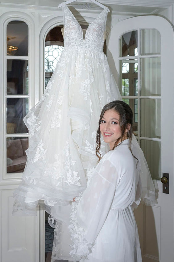 Bride standing next to her wedding dress hanging in the bridal suite.