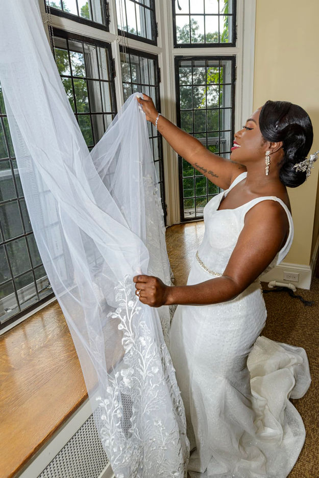 Bride looking at her wedding veil in soft window light