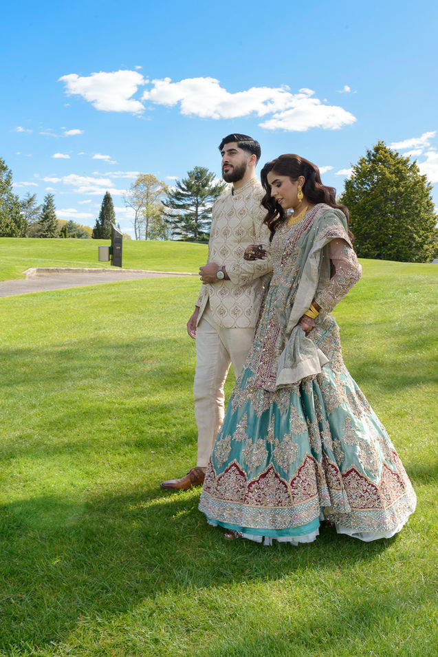 Beautiful bride and groom in traditional Pakistani attire arm and arm walking through a field. Wedding Photography by Ron Richman