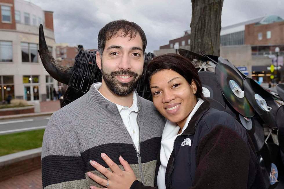 engaged-couple-in-harvard-square-standing-smiling-in-front-of-a-bull-sculpture.jpg