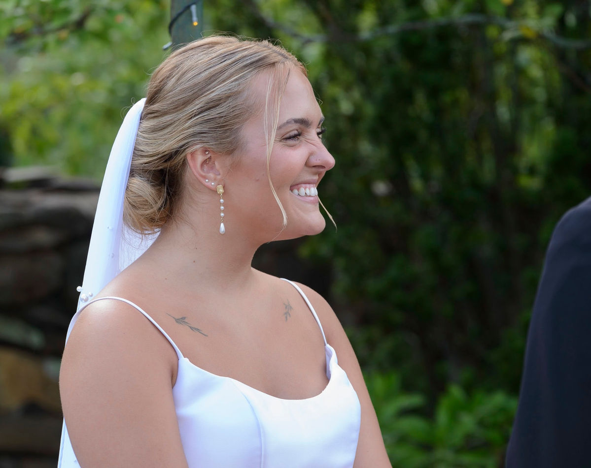 Close-up of bride smiling during ceremony outdoors.