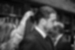 Black and white candid wedding photo of groom getting hair fixed showing light, texture, and emotion.