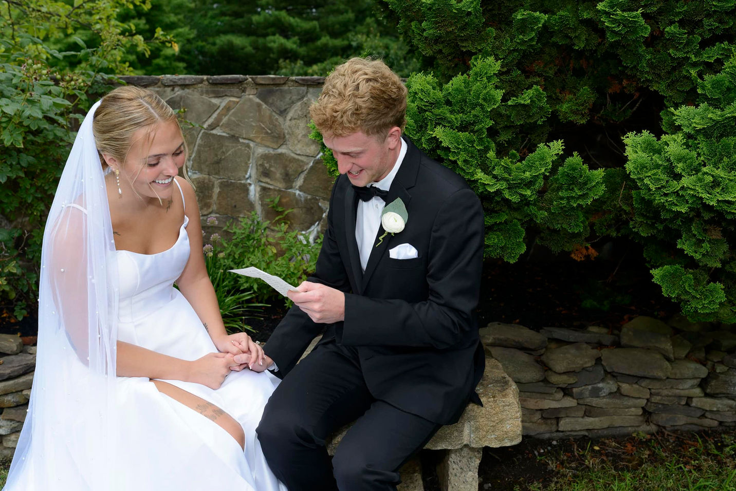 Bride and groom reading vows and laughing together outside.