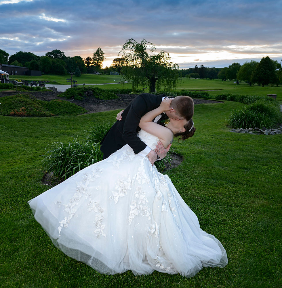 Bride and groom share a sunset kiss on a green lawn during their wedding portraits.