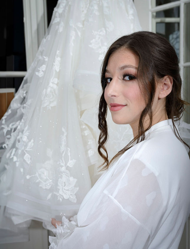 Vertical portrait of bride standing next to her wedding dress.