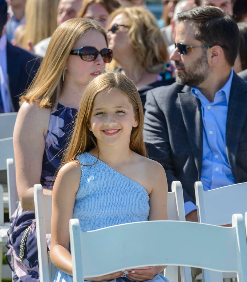 Cute young girl guest sits smiling at the camera in a light blue top.
