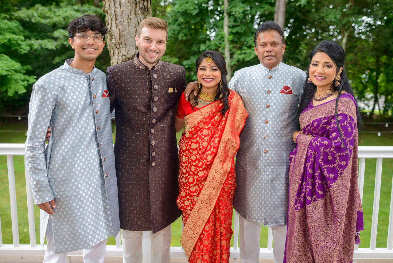 Bride and groom posing with family members on the outdoor deck in traditional red, silver, purple and brown Indian wedding attire.