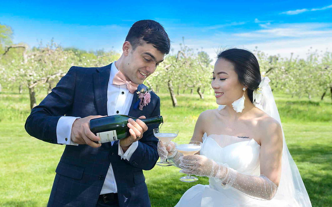 Bride and groom have a champagne toast in an apple orchard during a spring wedding. portrait.