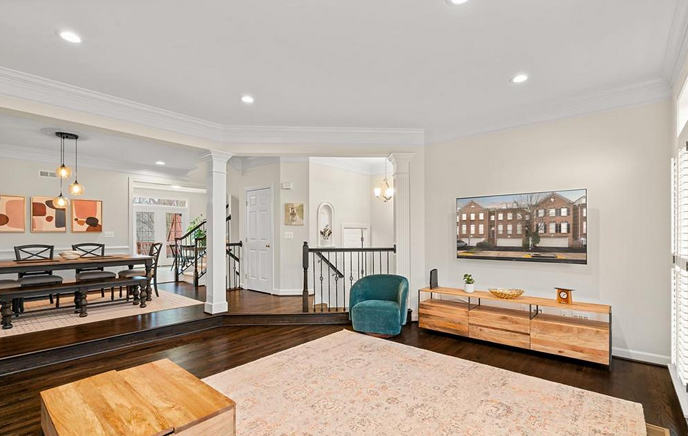 Spacious living room with modern decor, teal chair, wood furniture, and wall art. Dining area with pendant lights. Neutral tones, bright ambiance.