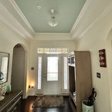 A hallway with a white door, side window panels, and a pale blue ceiling. A lamp and decor sit on a dresser. Soft lighting creates a cozy mood.