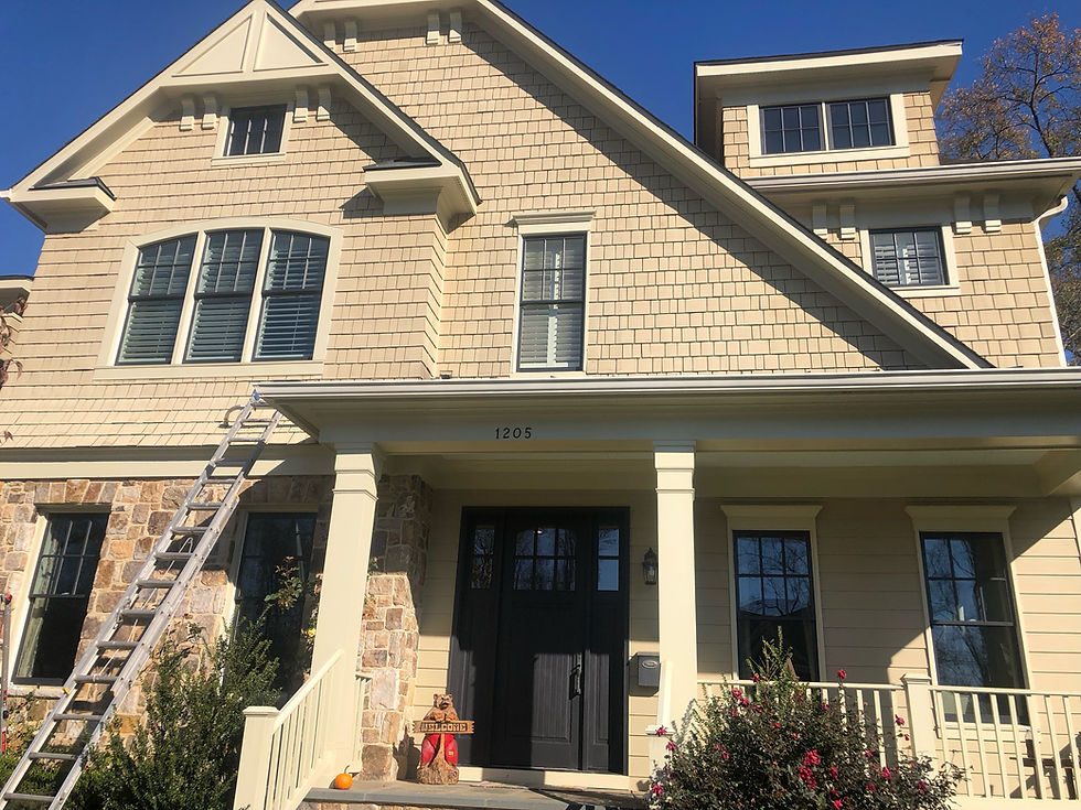 Beige house with ladder against it, stone and wood siding, porch with dog statue and "Welcome" sign. Clear blue sky background.