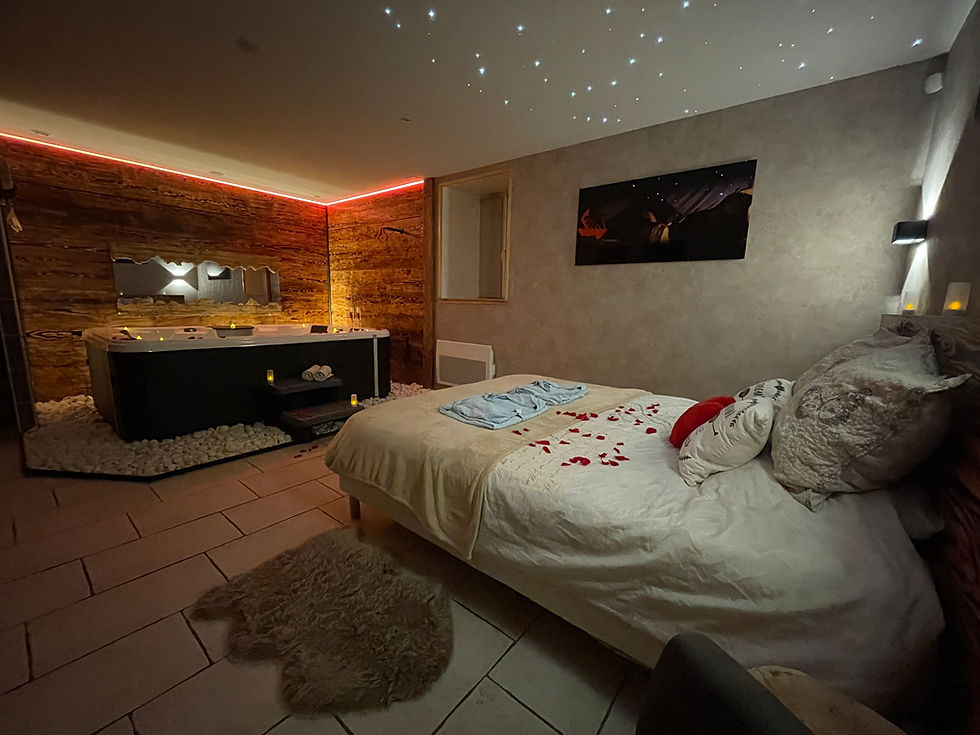Chambre romantique avec jacuzzi, lit décoré de pétales rouges, éclairage tamisé, plafond étoilé, ambiance chaleureuse et intime.