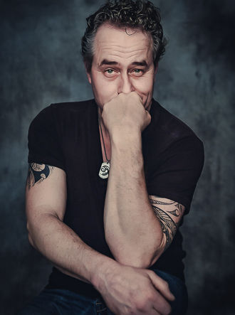 Man met tattoos poseert zittend met hand voor mond