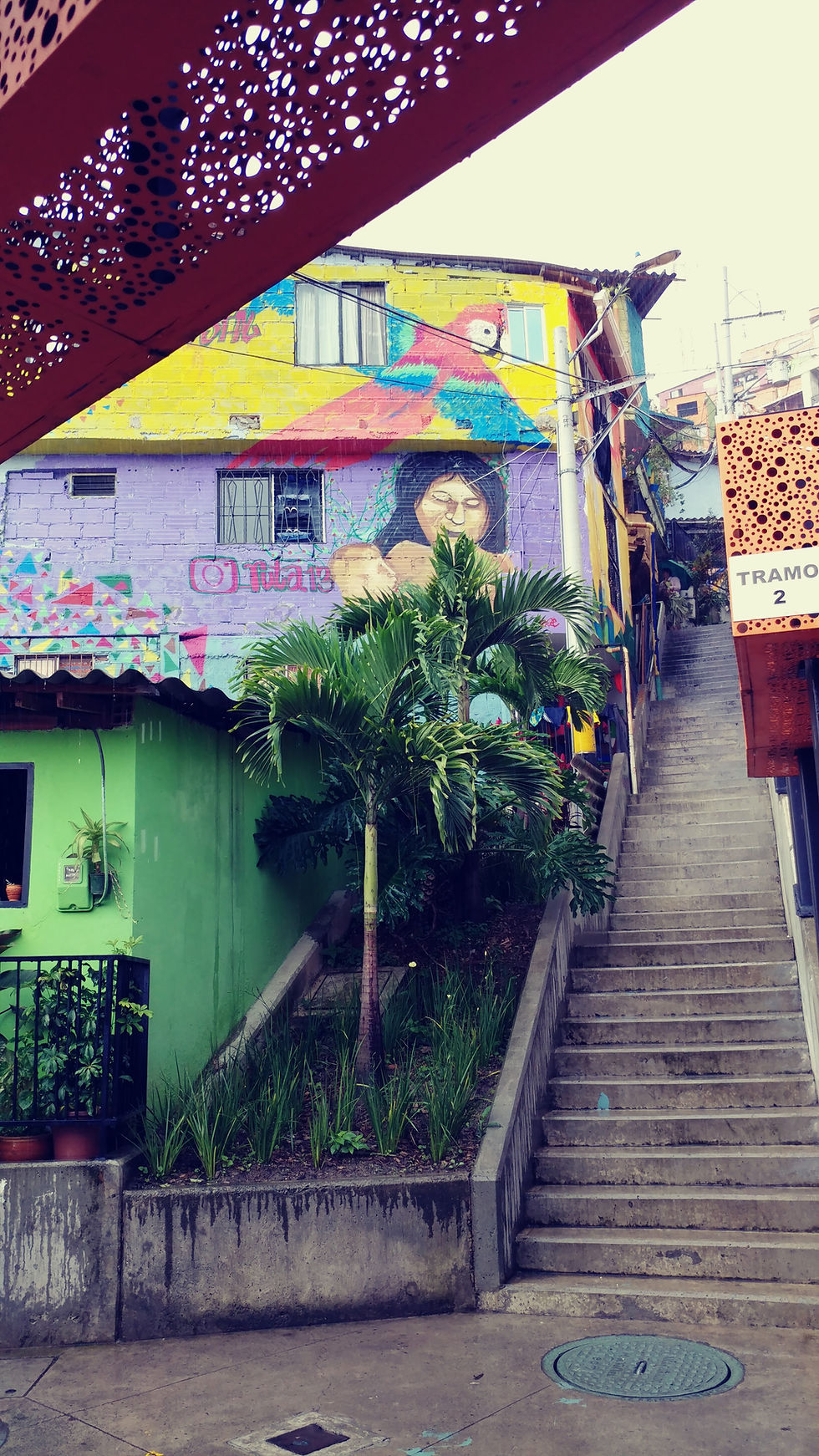 Colorful murals and a steep concrete staircase in Comuna 13, Medellín, Colombia, surrounded by tropical greenery.