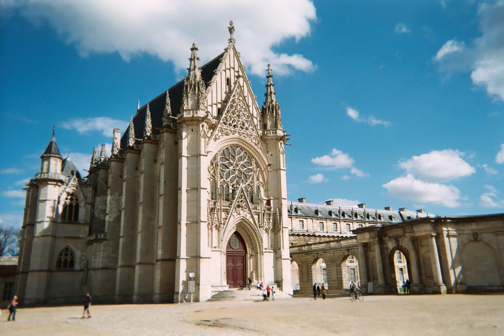 Gothic façade of the Sainte-Chapelle de Vincennes, featuring an ornate rose window and pointed arch entrance beneath a bright blue sky.