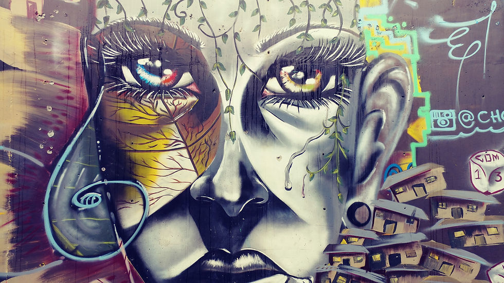 Colorful street art mural of a woman’s face with expressive eyes and hillside homes in Comuna 13, Medellín, Colombia.