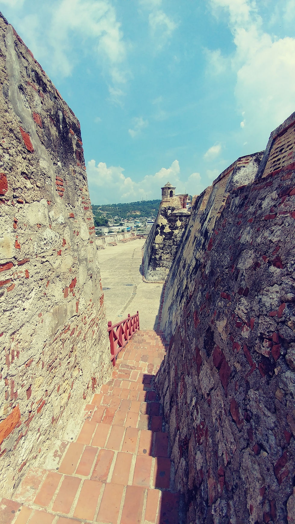 Historic stone fortification overlooking the Caribbean Sea in Cartagena, Colombia, with modern high-rise buildings visible along the coastline.