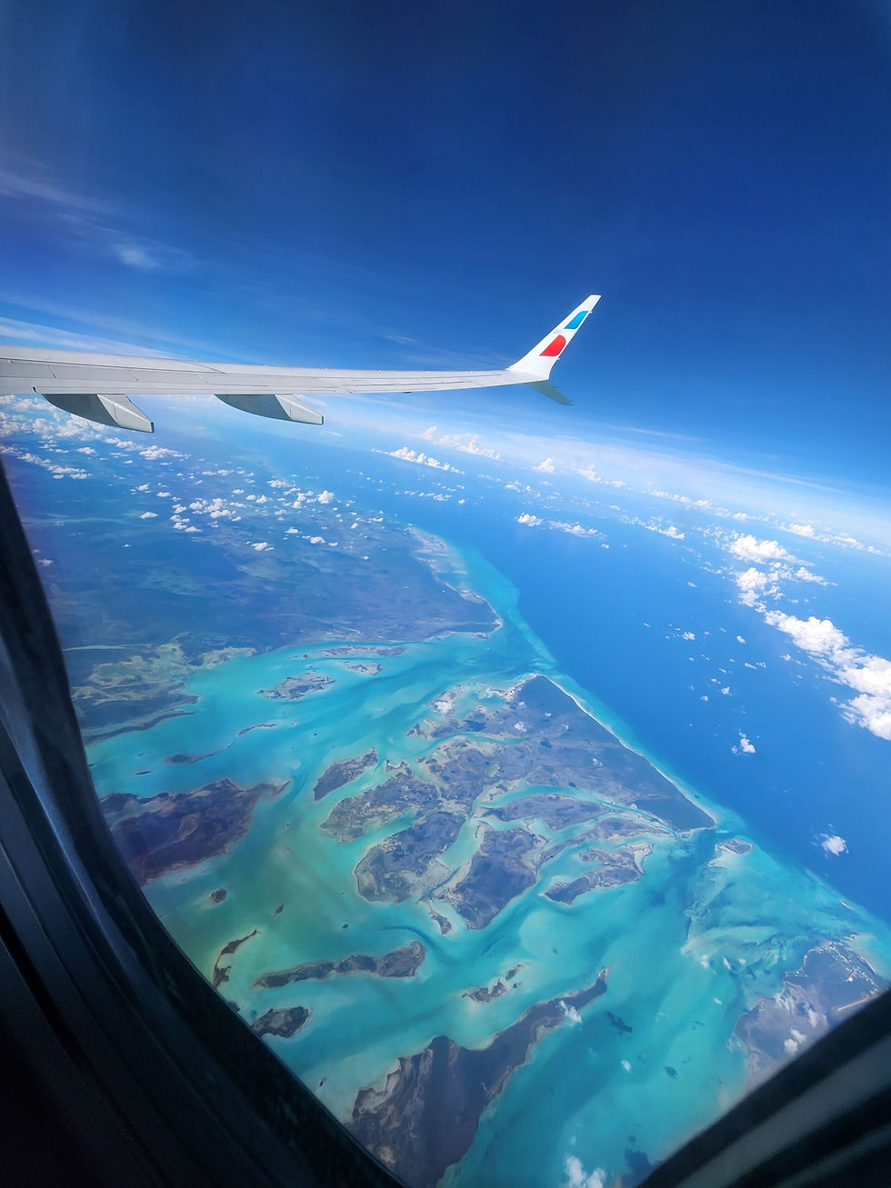 Aerial view of Mangrove Cay, Bahamas, with turquoise waters and islands seen from an airplane window.
