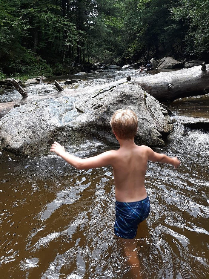 boy wearing blue swim trunks walks through river