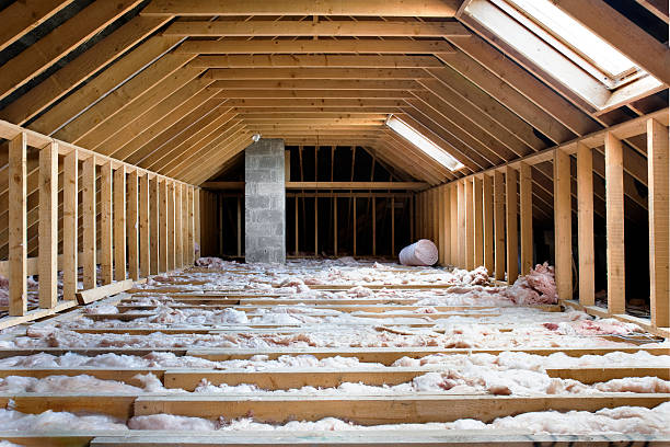 Unfinished attic with exposed wooden beams, insulation on the floor, and skylights. Bright, airy space with a roll of pink insulation.