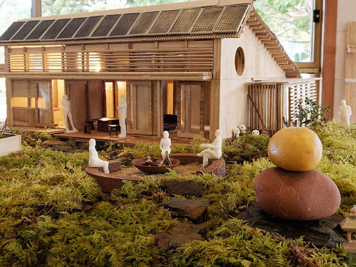 Architectural model of a wooden house with solar panels, surrounded by grass and figures, capturing a serene, natural scene.