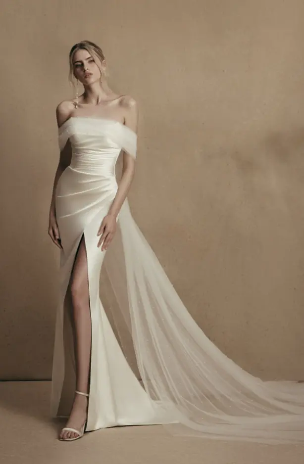 Schlichtes, figurbetontes Hochzeitskleid aus Mikado mit strukturiertem Oberteil und asymmetrischem Drapé-Effekt auf der Hüfte. Zeitlos und skulptural zugleich – ideal für stilbewusste Bräute.
