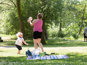 Lady in pink top and black shorts throwing a ball to a blonde haired child
