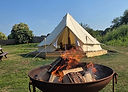 Fire pit with burning logs in it, cream bell tent in background