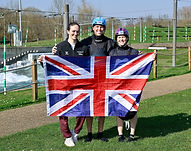 Mallory Franklin, Joe Clarke and Kimberly Woods holding a Union Jack in front of the course at Lee Valley White Water Centre