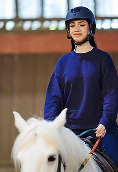 Lady on a white horse wearing blue top and riding hat