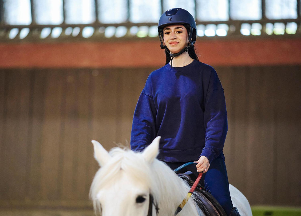 Person riding a while horse in the indoor menage at Lee Valley Riding Centre