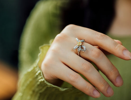 Fine jewelry ring featuring a yellow diamond and petal-shaped white diamonds on model's hand.