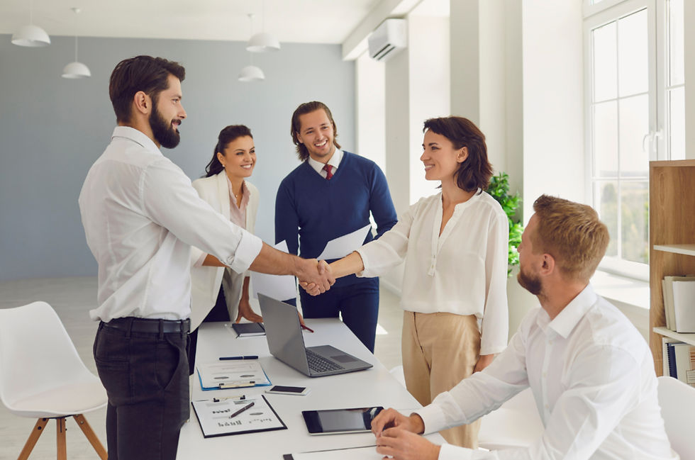 People in business attire shake hands in a bright office. Others smile, holding papers. A laptop and documents are on the table. They have found their content writer!