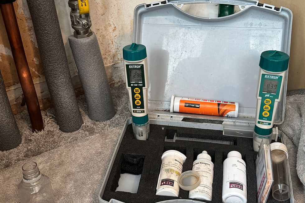 Open case with EXTECH water test meters and reagent bottles beside insulated pipes in a basement, suggesting a plumbing check.